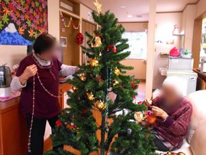 クリスマスツリーの飾り付けをする入居者と職員